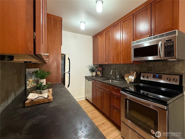 2328 10th Ave E Unit 102, Seattle, WA 98102 - kitchen featuring stainless steel appliances, dark countertops, backsplash, light wood-style floors, and brown cabinetry