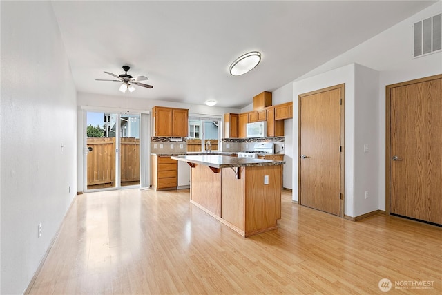 8803 136th St E, Puyallup, WA 98373 - kitchen featuring white appliances, light wood finished floors, a center island, and backsplash