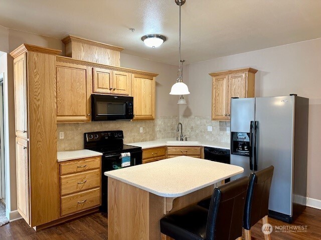 1548 River Rd Unit 105, Longview, WA 98632 - kitchen featuring black appliances, backsplash, light countertops, a kitchen island, and dark wood-type flooring