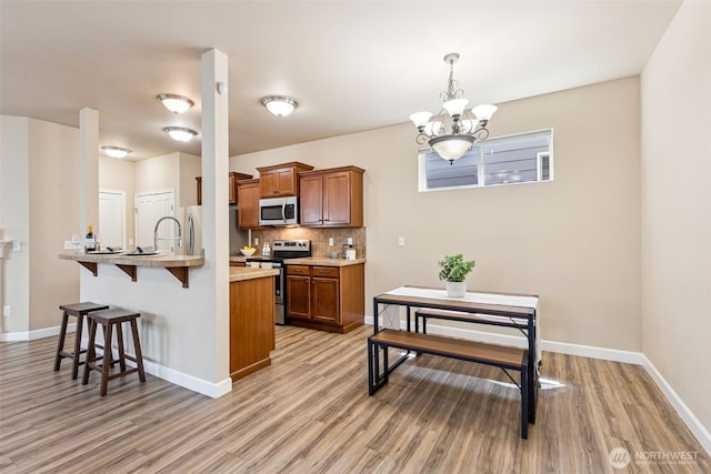 4444 Edgewater Blvd NE, Lacey, WA 98516 - kitchen with appliances with stainless steel finishes, a breakfast bar area, brown cabinets, light wood-style floors, and a chandelier