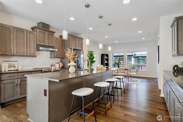 935 7th Ave NE Unit 17.3, Issaquah, WA 98029 - kitchen with under cabinet range hood, a breakfast bar area, dark wood-style floors, decorative backsplash, and recessed lighting