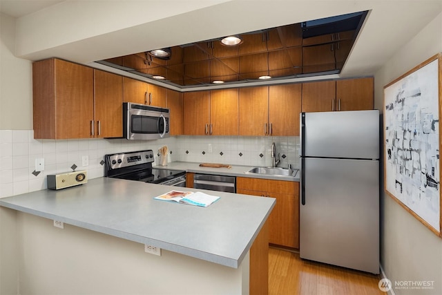 905 Cherry St Unit 101, Seattle, WA 98104 - kitchen with appliances with stainless steel finishes, brown cabinets, a peninsula, light countertops, and light wood-style floors