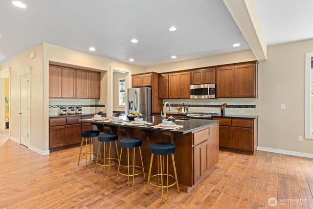 1635 Tannerwood Way SE, North Bend, WA 98045 - kitchen featuring stainless steel appliances, dark countertops, backsplash, a breakfast bar area, and light wood-style flooring