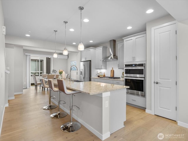 509 237th Pl SE Unit D, Bothell, WA 98021 - kitchen with wall chimney range hood, appliances with stainless steel finishes, a breakfast bar, recessed lighting, and light wood-type flooring