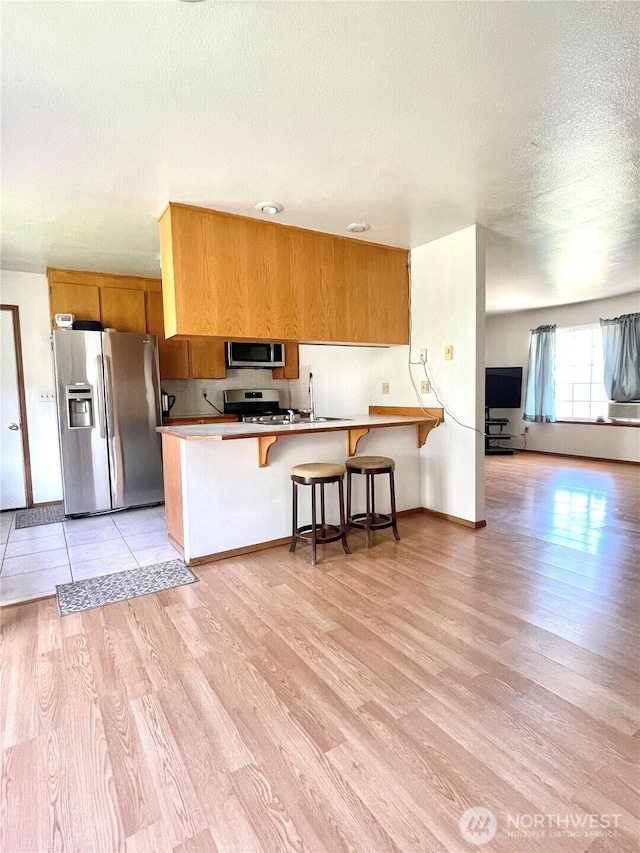 59G Copple Rd, Omak, WA 98841 - kitchen featuring appliances with stainless steel finishes, a peninsula, light wood finished floors, brown cabinets, and a textured ceiling