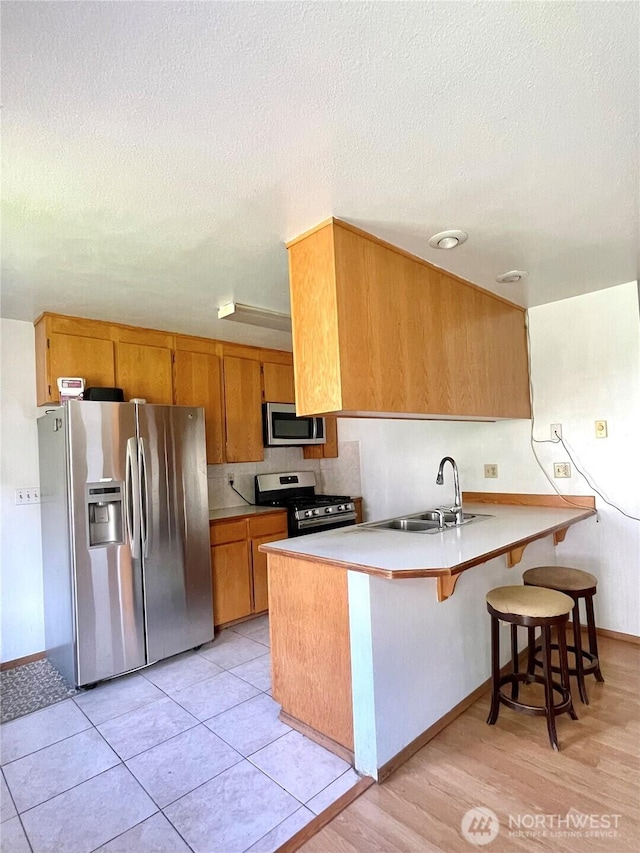 59G Copple Rd, Omak, WA 98841 - kitchen featuring appliances with stainless steel finishes, a peninsula, brown cabinetry, light countertops, and a kitchen bar