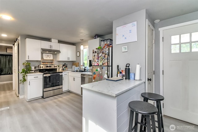 19820 63rd Avenue Ct E, Spanaway, WA 98387 - kitchen featuring appliances with stainless steel finishes, under cabinet range hood, a peninsula, white cabinets, and a kitchen bar
