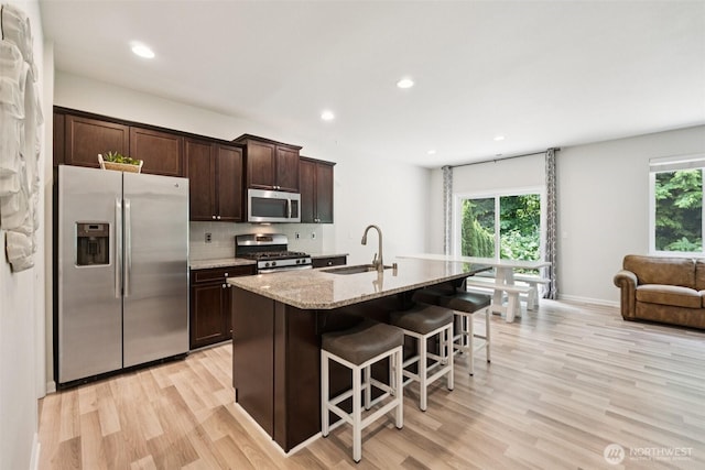 7608 16th Pl SE, Lake Stevens, WA 98258 - kitchen with stainless steel appliances, light wood-style flooring, a breakfast bar, dark brown cabinets, and decorative backsplash