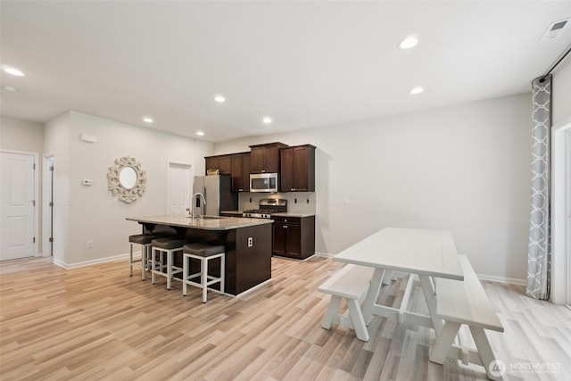 7608 16th Pl SE, Lake Stevens, WA 98258 - kitchen featuring stainless steel appliances, a center island with sink, dark brown cabinets, a kitchen breakfast bar, and light wood-type flooring