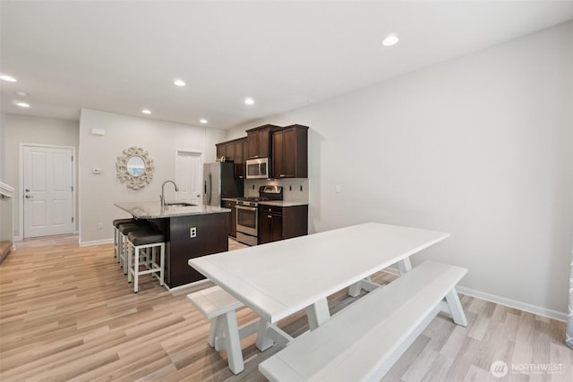 7608 16th Pl SE, Lake Stevens, WA 98258 - kitchen with appliances with stainless steel finishes, a center island with sink, light wood-style flooring, a breakfast bar, and dark brown cabinets