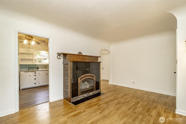 6711 100th St SW, Lakewood, WA 98499 - unfurnished living room featuring arched walkways, wood finished floors, a ceiling fan, and a tiled fireplace