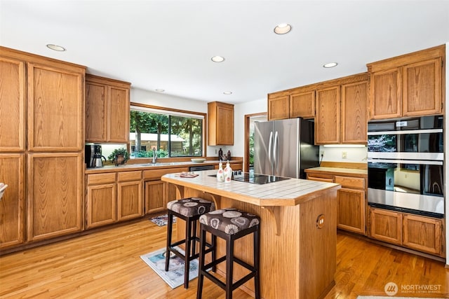 24131 SE 225th St, Maple Valley, WA 98038 - kitchen featuring appliances with stainless steel finishes, tile countertops, brown cabinetry, a breakfast bar, and recessed lighting