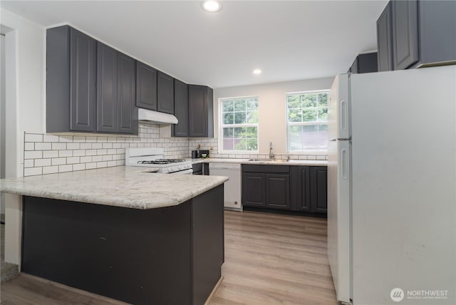 21405 Thompson Creek Rd SE, Tenino, WA 98589 - kitchen with white appliances, under cabinet range hood, a peninsula, light wood-style flooring, and decorative backsplash