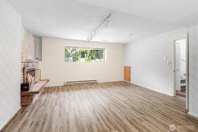 3909 Fielding Ave, Bellingham, WA 98229 - empty room featuring a baseboard heating unit, wood finished floors, track lighting, and a brick fireplace