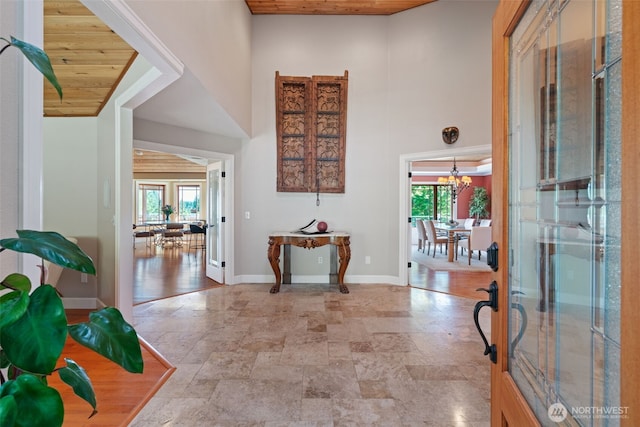 foyer featuring plenty of natural light, stone tile floors, a towering ceiling, a chandelier, and wood ceiling