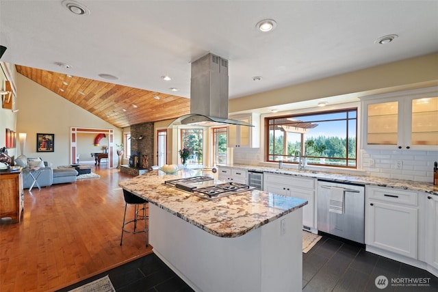 kitchen with stainless steel appliances, island exhaust hood, open floor plan, white cabinets, and glass insert cabinets