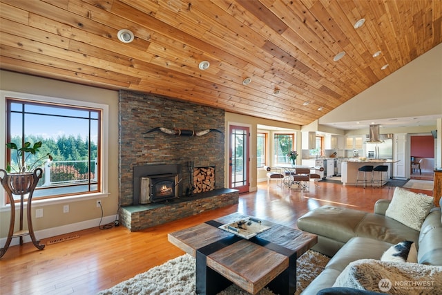 living area with healthy amount of natural light, vaulted ceiling, light wood-style floors, and a wood stove
