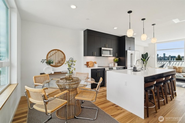 511 Howe St Unit C, Seattle, WA 98109 - kitchen featuring dark cabinetry, stainless steel appliances, light countertops, light wood-style floors, and a center island with sink