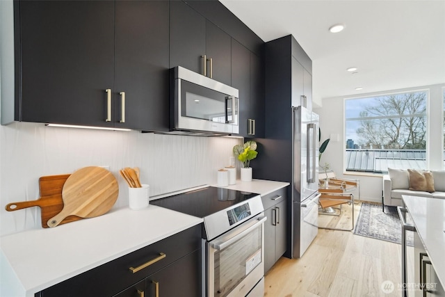 511 Howe St Unit C, Seattle, WA 98109 - kitchen with stainless steel appliances, dark cabinetry, light wood-style flooring, light countertops, and recessed lighting