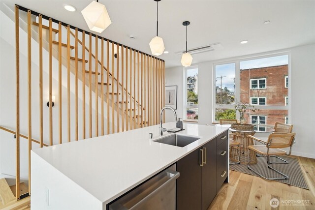 511 Howe St Unit C, Seattle, WA 98109 - kitchen with stainless steel dishwasher, light wood finished floors, a kitchen island with sink, hanging light fixtures, and light countertops