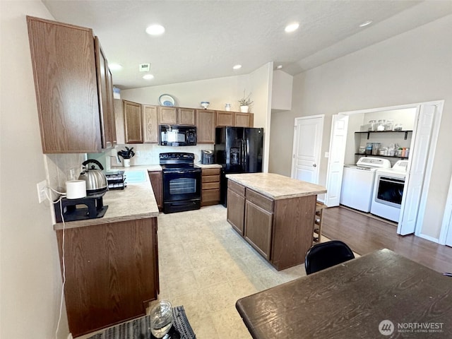 314 SW Homestead, College Place, WA 99324 - kitchen featuring black appliances, independent washer and dryer, vaulted ceiling, light countertops, and a center island