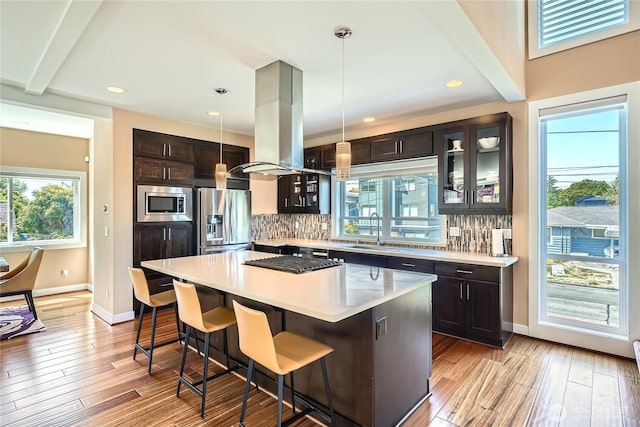9544 3rd Ave NW, Seattle, WA 98117 - kitchen with appliances with stainless steel finishes, island range hood, a kitchen breakfast bar, glass insert cabinets, and decorative backsplash