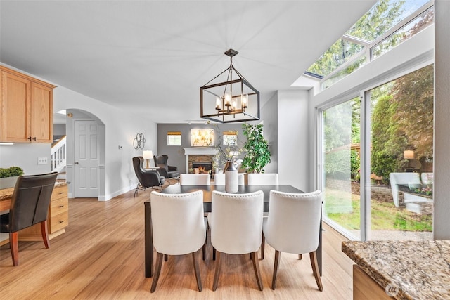 22418 SE 281st St, Maple Valley, WA 98038 - dining space featuring arched walkways, a stone fireplace, light wood-style flooring, stairs, and a chandelier