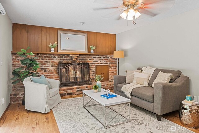 29701 52nd Ave E, Graham, WA 98338 - living area featuring light wood-style flooring, a fireplace, ceiling fan, an AC wall unit, and wooden walls
