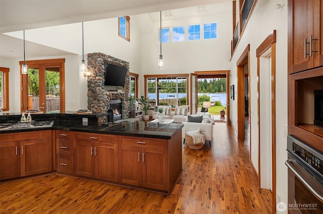 10904 W Lake Joy Dr NE, Carnation, WA 98014 - kitchen with oven, open floor plan, brown cabinetry, a stone fireplace, and a high ceiling