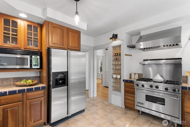 4628 Sunnyside Ave N, Seattle, WA 98103 - kitchen with appliances with stainless steel finishes, wall chimney range hood, tile countertops, brown cabinets, and glass insert cabinets