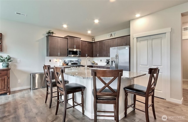 7804 208th Ave E, Bonney Lake, WA 98391 - kitchen with stainless steel appliances, dark brown cabinetry, light wood-style flooring, light stone countertops, and a breakfast bar