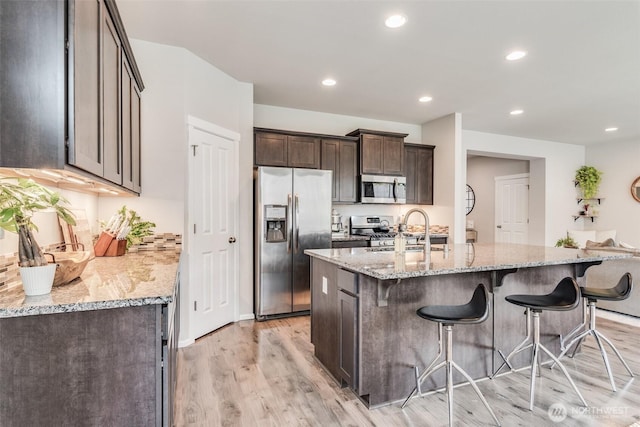 2726 Kacie Ct NE, Lacey, WA 98516 - kitchen with appliances with stainless steel finishes, dark brown cabinetry, light wood-style floors, a breakfast bar, and light stone countertops