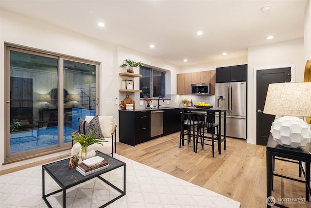 9047 Dibble Ave NW Unit C, Seattle, WA 98117 - kitchen featuring appliances with stainless steel finishes, dark cabinetry, open shelves, light wood-style floors, and recessed lighting