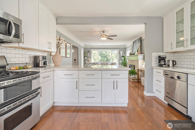 5253 35th Ave SW, Seattle, WA 98126 - kitchen with appliances with stainless steel finishes, a peninsula, a ceiling fan, light wood finished floors, and white cabinetry