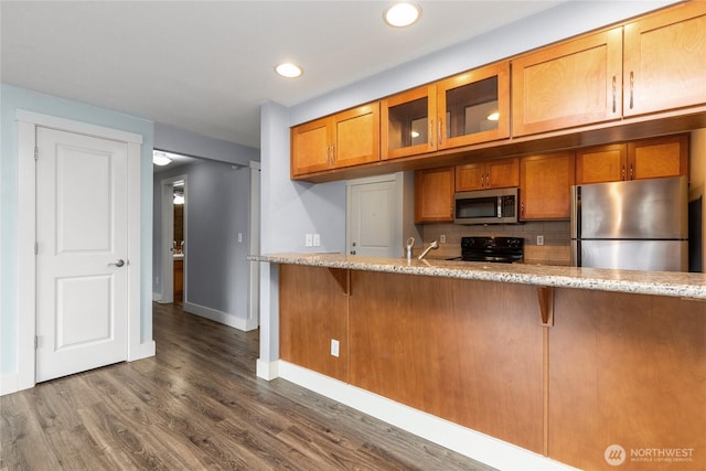25 N Broadway Unit 207, Tacoma, WA 98403 - kitchen with appliances with stainless steel finishes, brown cabinetry, tasteful backsplash, glass insert cabinets, and dark wood-style flooring