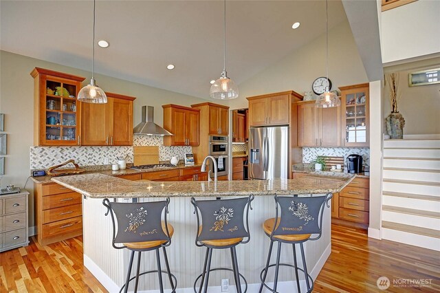 656 Lehman Dr, Camano Island, WA 98282 - kitchen featuring stainless steel appliances, wall chimney range hood, brown cabinetry, light wood-style flooring, and lofted ceiling
