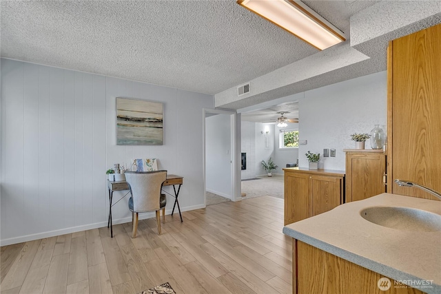1728 N James St, Tacoma, WA 98406 - kitchen with light wood-type flooring, a textured ceiling, light countertops, a ceiling fan, and brown cabinets