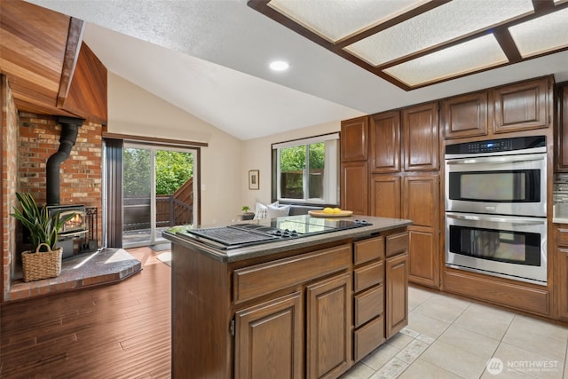 8037 Incline Dr SE, Olympia, WA 98513 - kitchen featuring stainless steel double oven, a wood stove, stovetop with downdraft, vaulted ceiling, and a center island