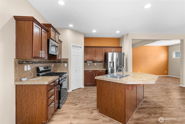 18328 73rd Avenue Ct E, Puyallup, WA 98375 - kitchen featuring appliances with stainless steel finishes, light wood finished floors, a kitchen island with sink, backsplash, and light countertops