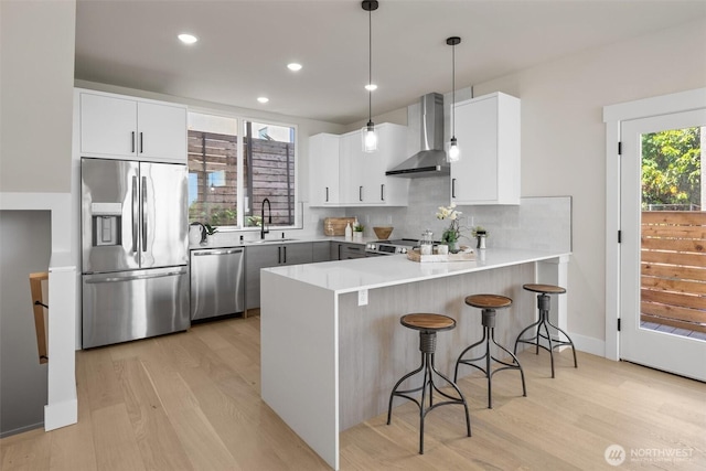 1313 14th Ave S Unit B, Seattle, WA 98144 - kitchen featuring wall chimney exhaust hood, stainless steel appliances, a peninsula, light wood-style flooring, and recessed lighting