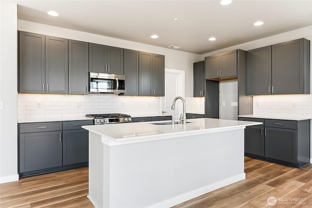 13936 178th St E Unit 85, Puyallup, WA 98374 - kitchen featuring stainless steel microwave, wood finished floors, a center island with sink, backsplash, and light countertops
