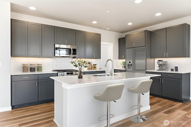 13936 178th St E Unit 85, Puyallup, WA 98374 - kitchen with stainless steel appliances, tasteful backsplash, light wood-style flooring, a center island with sink, and light countertops