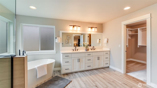 23000 SE Sycamore St, Black Diamond, WA 98010 - bathroom with double vanity, a freestanding bath, wood finished floors, a spacious closet, and recessed lighting