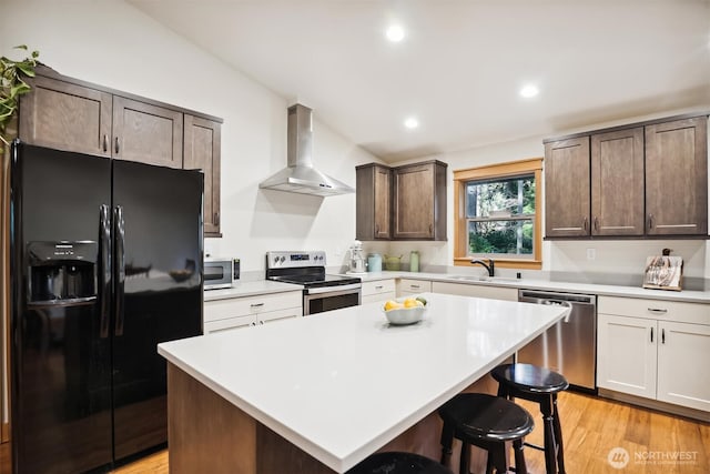 11211 Juniper Pl, Anderson Island, WA 98303 - kitchen featuring stainless steel appliances, wall chimney range hood, a breakfast bar, light countertops, and light wood-style floors