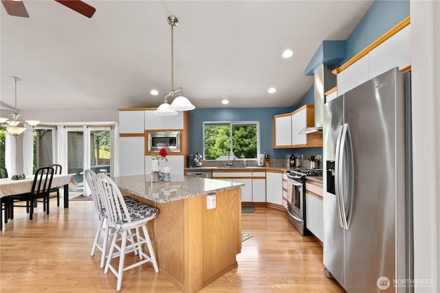 8615 176th St NW, Stanwood, WA 98282 - kitchen featuring appliances with stainless steel finishes, a kitchen island, white cabinets, light wood-style flooring, and hanging light fixtures