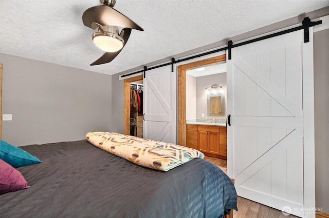 132 Tanglewood Dr, Longview, WA 98632 - bedroom with a barn door, light wood-style flooring, a textured ceiling, a walk in closet, and ensuite bath