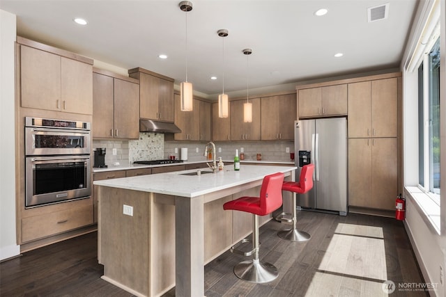 587 155th Pl NE, Bellevue, WA 98007 - kitchen with stainless steel appliances, dark wood-style flooring, under cabinet range hood, decorative backsplash, and a kitchen island with sink