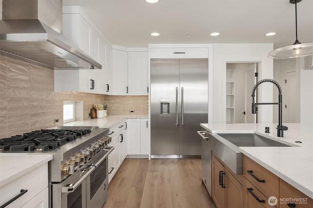 11216 NE 67th St Unit 4, Kirkland, WA 98033 - kitchen featuring wall chimney range hood, high quality appliances, light wood-style flooring, tasteful backsplash, and pendant lighting
