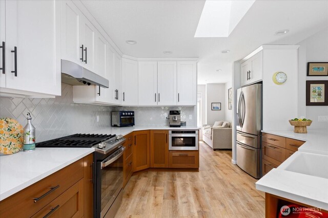 1043 NE Pennington Loop, Coupeville, WA 98239 - kitchen featuring appliances with stainless steel finishes, under cabinet range hood, light wood finished floors, light countertops, and a skylight