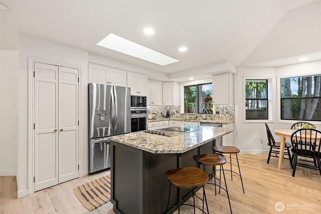 9019 166th St E, Puyallup, WA 98375 - kitchen with black appliances, a skylight, a kitchen bar, light wood-style floors, and a kitchen island